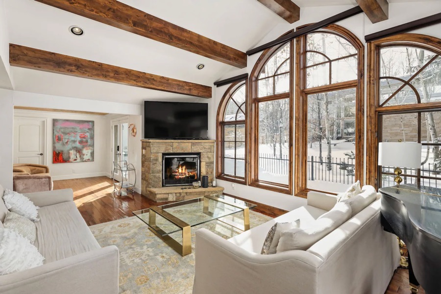 Living room fireplace lit, arched windows onto the snowy garden, grand piano at right.